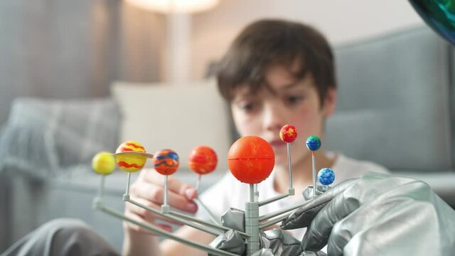 Father and son play in the living room at home, man in an astronaut costume sitting on the floor with her son, boy playing with a toy model of the solar system, study of astronomy, 4k slow motion.