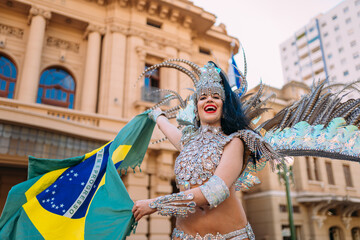 Beautiful Brazilian woman wearing colorful Carnival costume and Brazil flag during Carnaval street...