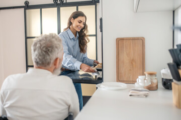 Obraz premium Gray-haired handicapped man and his young wife in the kitchen getting the breakfast ready