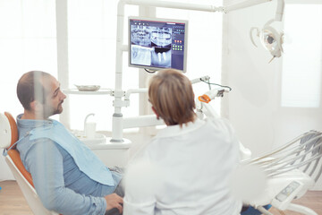 Obraz premium Dentist doctor and patient looking at digital teeh x-ray in stomatology hospital office. Sick patient sitting on dental chair preparing for dentistry surgery during somatology appointment