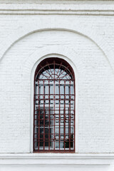 An old arched window behind bars in an old white brick building. Vertical.