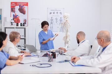 Hospital woman nurse presting bone structure using body anatomy skeleton discussing medical expertise. Physician team working in meeting room at healthcare treatment explaining health diagnosis