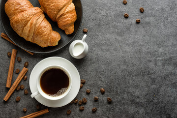 Cup of coffee and croissants on the table with cinnamon sticks and coffee beans.
