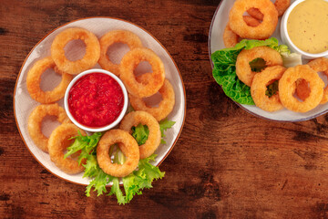 Calamari rings. Deep fried squid rings with green salad leaves and various dips, overhead flat lay shot on a dark rustic wooden background with a place for text
