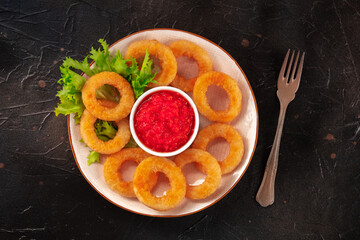 Calamari rings. Deep fried squid rings with lettuce leaves and tomato sauce, overhead shot on a black background