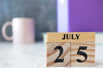 Cube wooden calendar showing date on 25 July. Wooden calendar with date on the table. blur objects on background