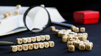 Creative writing lettering next to open textbook, magnifying glass, pen and red gift box. Concept...