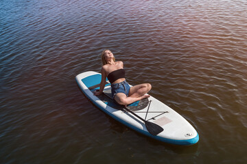 Fototapeta na wymiar Young female surfer lying on sup board and rest at nature