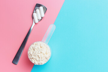 Protein scoop and capsules on pink and blue background close-up, top view.