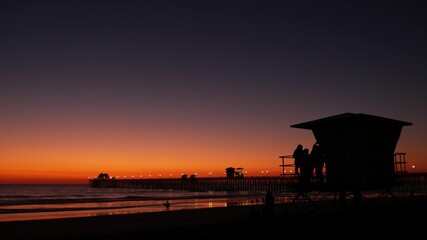 Young teen girls silhouettes near lifeguard tower, friends on pacific ocean beach, sunset dusk in...