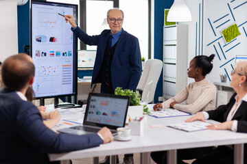 Experienced project leader analysing financial presentation during business conference in brainstorming room using digital devices. Multiethnical businesspeople working in professional startup