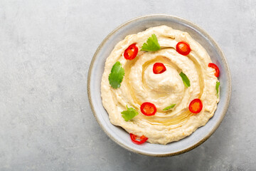 Hummus made from mashed chickpeas, tahini and lemon with olive oil, decorated with hot peper and coriander. On grey table. Top view.