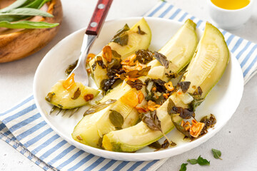 Stewed zucchini with herbs and garlic in a white plate on a gray concrete background. Summer recipes, vegan food, diet.