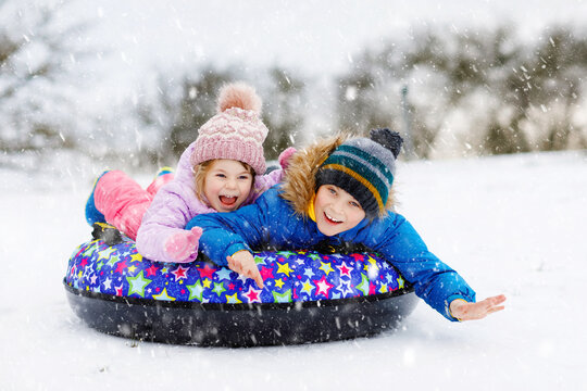 Active toddler girl and school boy sliding together down the hill on snow tube. Happy children, siblings having fun outdoors in winter on sledge. Brother and sister tubing snowy downhill, family time.