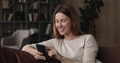 Beautiful millennial woman relaxing alone at home sit on sofa hold smartphone answer to friend texting sms use messenger, happy modern tech user enjoy new mobile app, make order, chat remotely concept
