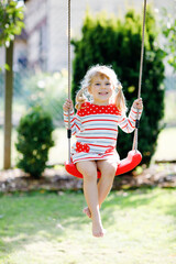 Happy beautiful little toddler girl having fun on swing in domestic garden. Cute healthy child...