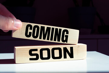 Coming Soon text on a wooden background and stack of coins.