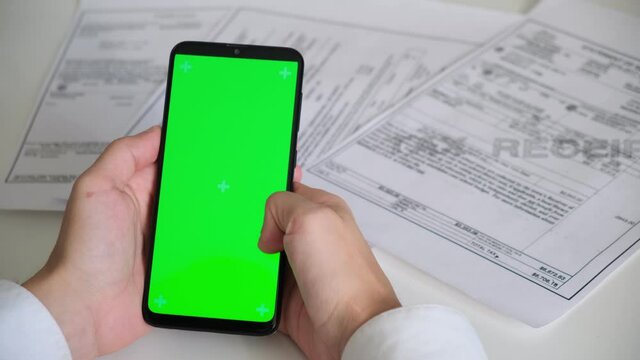 Phone with green screen and payment receipts, tax documents on white background top View . smartphone chromakey swipes in different directions. copy space. High quality 4k footage
