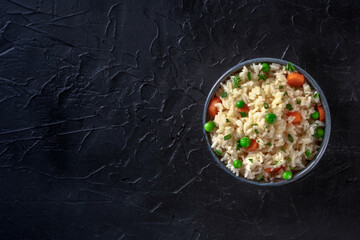 Rice with green peas, carrots, and scallions, overhead shot on a black background with copyspace