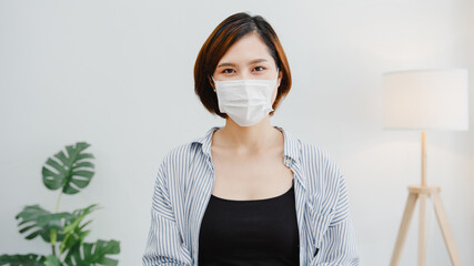 Asia businesswoman wear face mask social distancing in situation for virus prevention looking at camera smiling under surgical mask back to work in office workspace. Lifestyle after corona virus. - Powered by Adobe