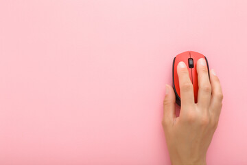 Young adult woman hand using red computer optical mouse on light pink table background. Pastel...