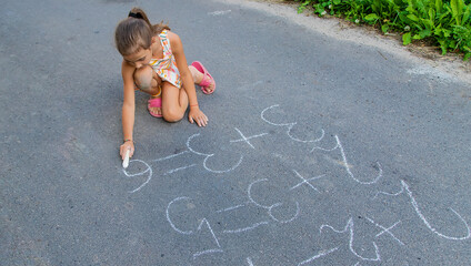 The child is doing chalk lessons on the asphalt. Selective focus.