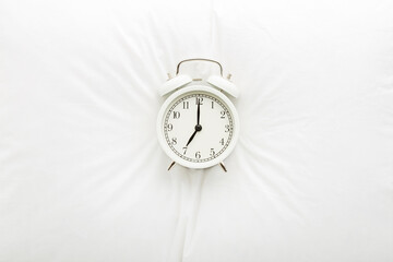 White alarm clock on pillow. 7 o'clock in morning. Waking time concept. Closeup. Top down view.