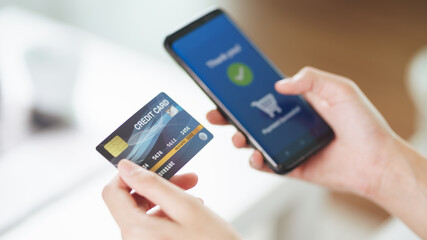 Young woman holding credit card and using smart phone for online shopping, internet banking, e-commerce, spending money, working from home concept