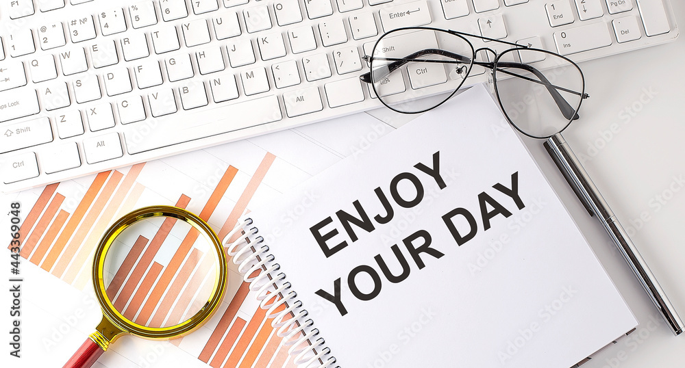 Poster enjoy your day text written on a notebook with keyboard, chart,and glasses