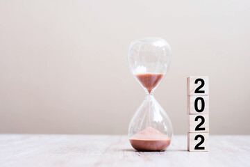 Hourglass with 2022 wooden cube blocks on table, Sand flowing through the bulb of Sandglass...