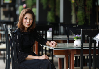 Beautiful cute Asian woman in black dress sitting alone in outdoor food shop and looking to camera