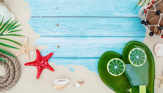 The concept of a holiday at the sea. Seashells, starfish, lime flip-flops and sand on a turquoise background. A picture for summer holidays with space for text. Top view.