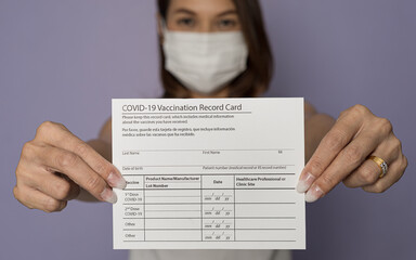 Selective focus on paper, vaccinated woman wearing medical mask holding showing Covid-19...