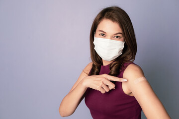 Vaccinated Asian woman wearing protective face mask point finger showing plaster bandage on arm after a coronavirus vaccine injection, Covid-19 vaccination, and antiviral Immunization concept