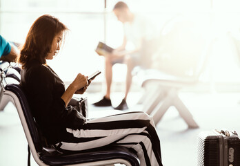 Woman sitting in airport lobby using smartphone and looking at screen while waiting for transit....