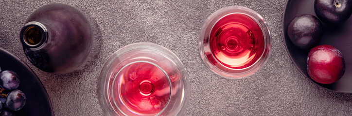 a bottle of red wine and flatlay glasses. plums on a textured table are gray concrete, a header for a website or a concept for a restaurant menu or decor