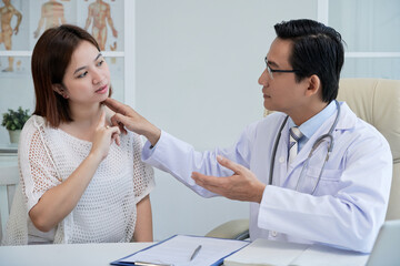 Physician touching neck of young woman suffering from chronic pain