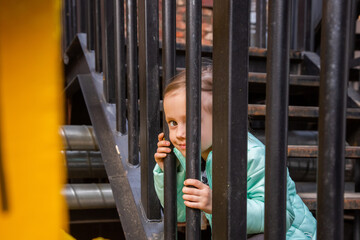 Adorable girl sits on the iron staircase with interest watching the passers-by