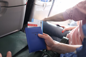 Man flying on plane and holding immunization passport against covid 19 and tickets closeup