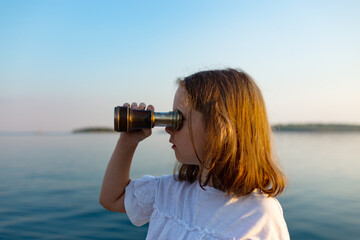 Funny little girl looking through vintage binoculars on sunny summer day. Rovinj town in background. Travel and adventure concept.