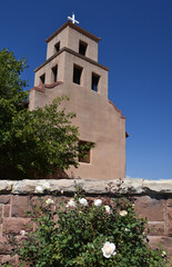 Fototapeta na wymiar the exterior of the historic church of our lady of guadalupe and red roses on a sunny fall day in santa fe, new mexico