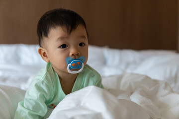 Portrait image of cute Asian Chinese 10 month old Asian Chinese baby boy with pacifier on bed