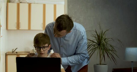 Young father supports and motivates his son. Boy works at his laptop and gets his fathers recognition.