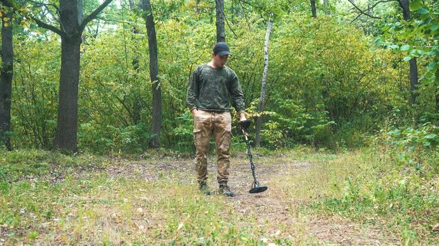 man walks with a metal detector through the forest