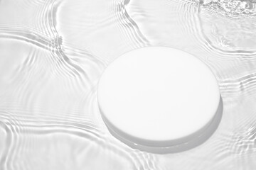 Empty white circle podium on transparent clear calm water texture with splashes and waves in...