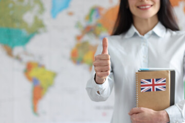 Woman holding english textbooks on background of world map and showing thumb up closeup