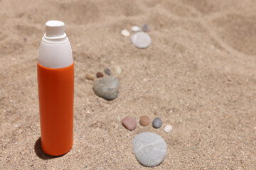 Orange jar of sunscreen standing on sand near stone footprints closeup