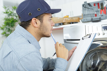 Naklejka na ściany i meble young serviceman with clipboard looking at washing machine