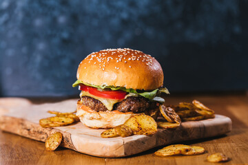 Classical burger with potato wedges on a wooden board with dark blue background - obrazy, fototapety, plakaty