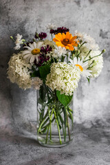 Bouquet of summer flowers of hydrangeas, daisies, cornflowers in a glass vase on a gray background